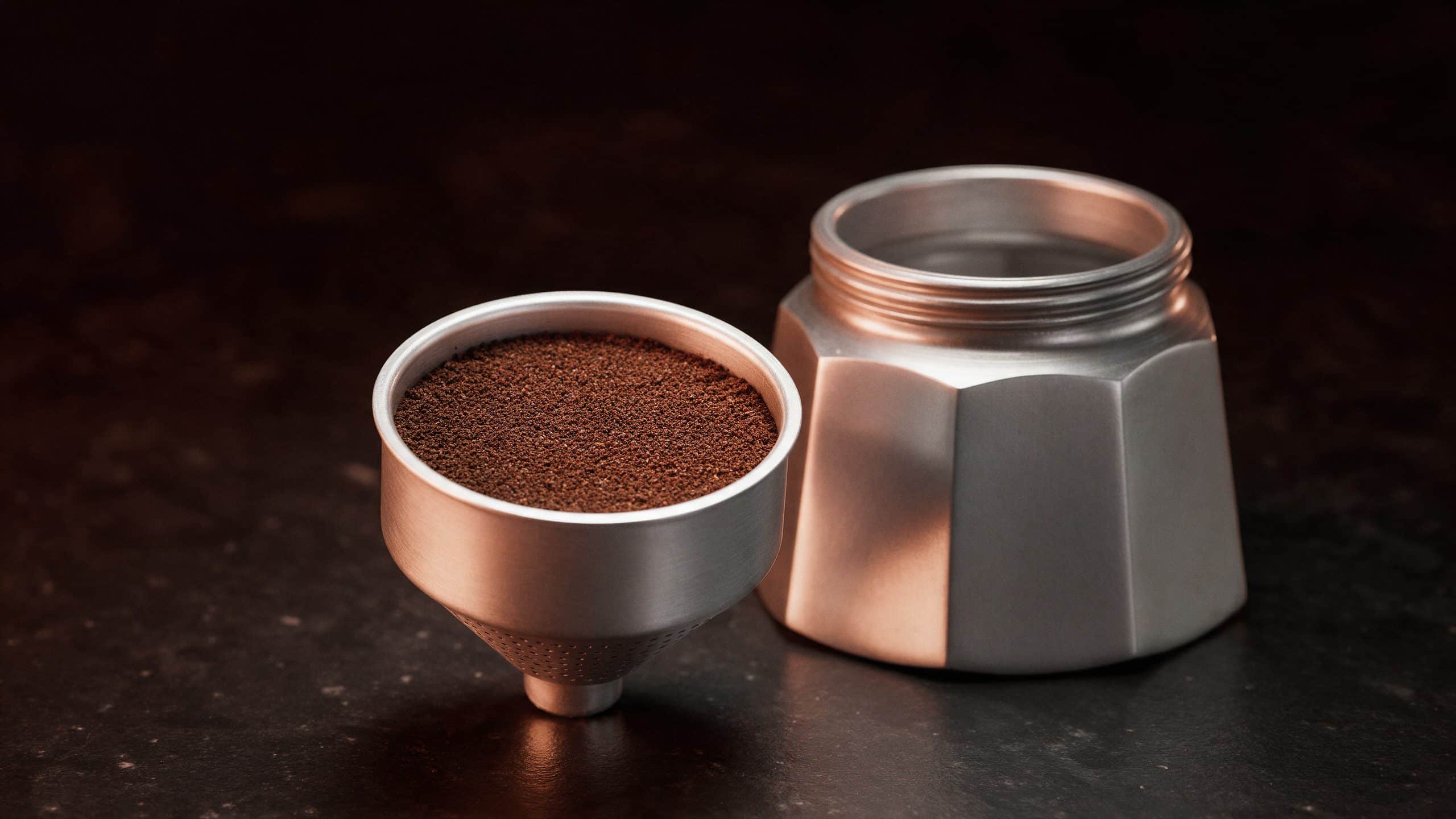 Moka pot filter funnel filled level with medium ground coffee beside the aluminum pot base